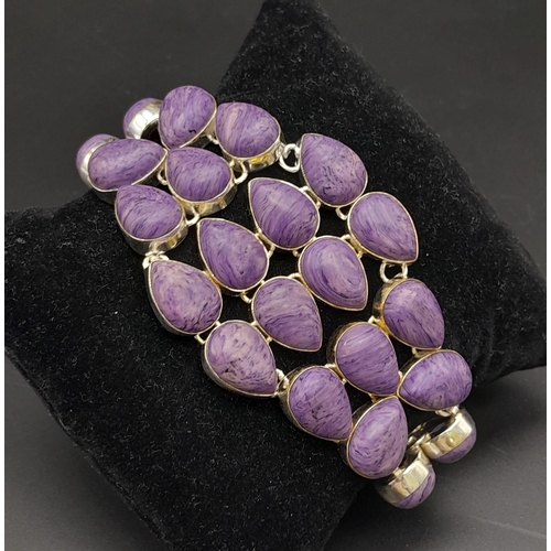 230 - A glorious, white metal (untested), bracelet with numerous, oval charoite cabochons. In a presentati... 