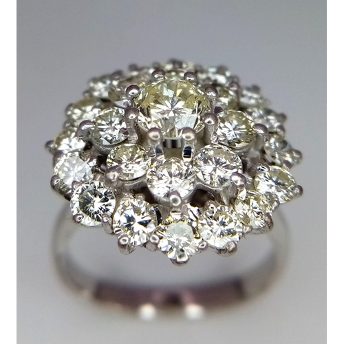 213 - An 18K White Gold Diamond Floral Ring. Central brilliant cut diamond with a two row halo of round cu... 