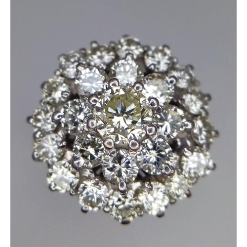 213 - An 18K White Gold Diamond Floral Ring. Central brilliant cut diamond with a two row halo of round cu... 