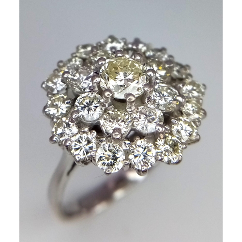 213 - An 18K White Gold Diamond Floral Ring. Central brilliant cut diamond with a two row halo of round cu... 