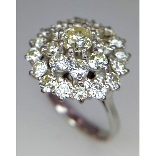 213 - An 18K White Gold Diamond Floral Ring. Central brilliant cut diamond with a two row halo of round cu... 