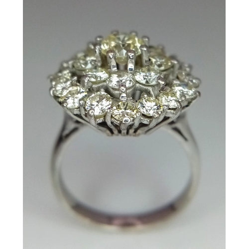 213 - An 18K White Gold Diamond Floral Ring. Central brilliant cut diamond with a two row halo of round cu... 