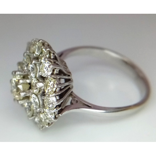 213 - An 18K White Gold Diamond Floral Ring. Central brilliant cut diamond with a two row halo of round cu... 