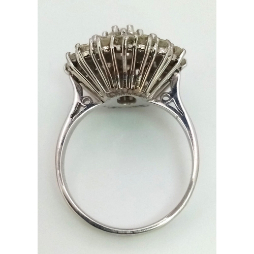 213 - An 18K White Gold Diamond Floral Ring. Central brilliant cut diamond with a two row halo of round cu... 