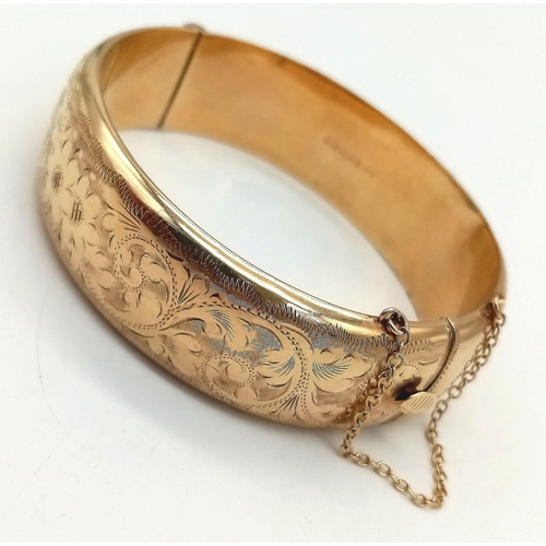 599 - A 9K GOLD HINGED BANGLE WITH SAFETY CHAIN , FLORAL DECORATION TO ONE SIDE AND SMALL DENT.  a/f    23... 