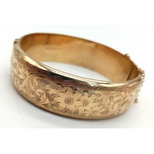 599 - A 9K GOLD HINGED BANGLE WITH SAFETY CHAIN , FLORAL DECORATION TO ONE SIDE AND SMALL DENT.  a/f    23... 