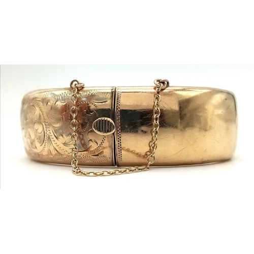 599 - A 9K GOLD HINGED BANGLE WITH SAFETY CHAIN , FLORAL DECORATION TO ONE SIDE AND SMALL DENT.  a/f    23... 