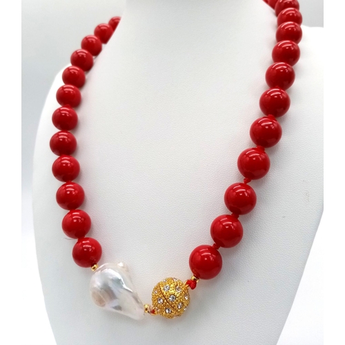 659 - A Red Coral And Baroque Pearl Necklace. 12mm beads with a large irregular shaped baroque pearl inter... 