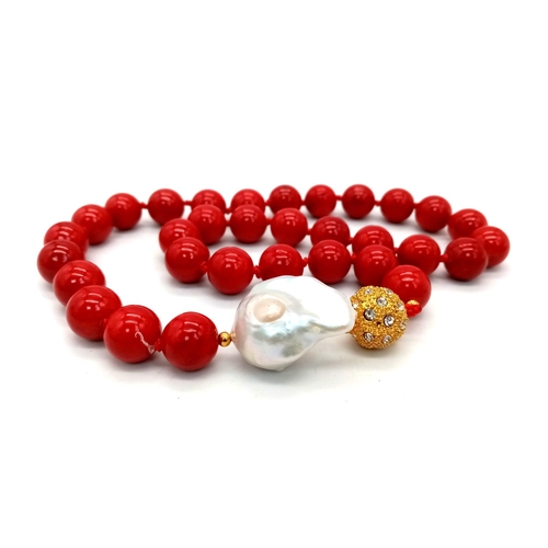 659 - A Red Coral And Baroque Pearl Necklace. 12mm beads with a large irregular shaped baroque pearl inter... 