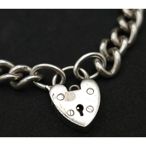 1016 - A Sterling silver chunky charm bracelet with heart padlock fastening. 31.6g