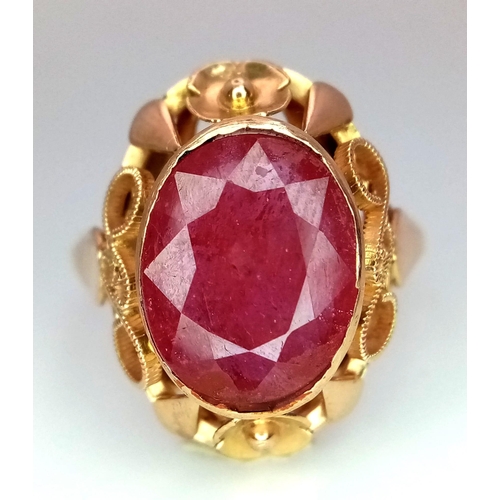 353 - A Vintage 18K Yellow Gold Ruby Ring. Central faceted oval ruby (5ct) in a raised decorative scroll f... 