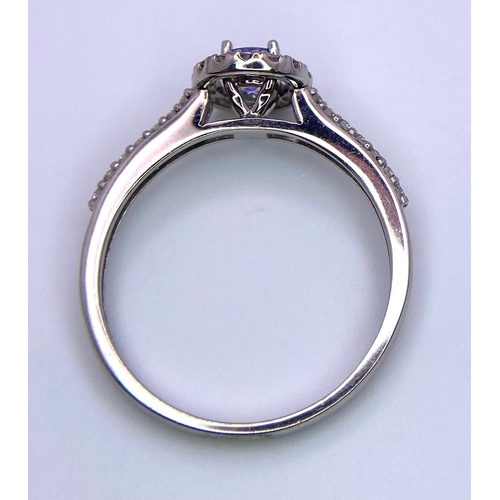 249 - An 18K White Gold Tanzanite and Diamond Ring. Central round cut tanzanite with diamond halo and shou... 