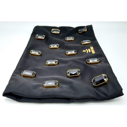 293 - A Prada Black Jewel Clutch. Textile exterior embellished with black stones. Gold toned hardware and ... 