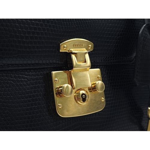 213 - Black Gucci Top Handle Bag.
Exotic, shiny lizard leather featuring gold toned hardware, flip-lock cl... 