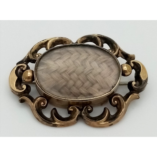 311 - An Antique 9K Yellow Gold (tested) Memorial/Mourning Brooch. Hair encapsulation centre with a scroll... 