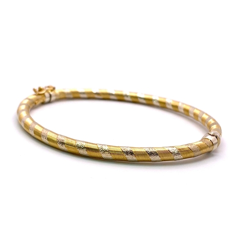 114 - A 9K Yellow and White Gold Clip-Open Bangle. Diagonal golden lines with white gold decorative bands.... 