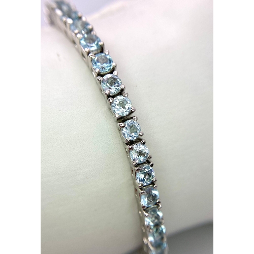 1303 - A Blue Topaz Tennis Bracelet. Round cut topaz gemstones set in 925 silver. 18cm length. 21.5g total ... 