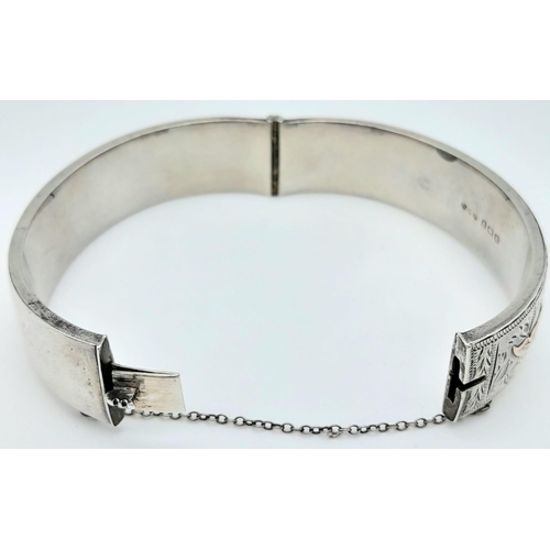 679 - A Sterling Silver Engraved Hinged Bangle with Safety Chain. 22.8g total weight.