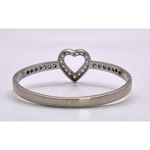 232 - An 18K White Gold and Diamond Heart Bangle. Central diamond round cut heart with diamonds on wings. ... 