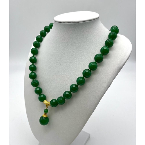 384 - An Entrancing Green Jade Necklace with Pendant Drop. 12mm rich green beads with a gilded jade ball d... 