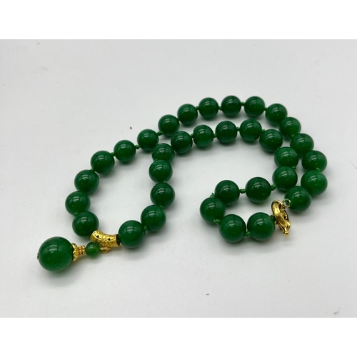 384 - An Entrancing Green Jade Necklace with Pendant Drop. 12mm rich green beads with a gilded jade ball d... 