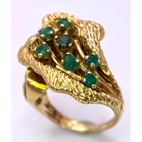 100 - A Vintage 18K Gold (tested) and Emerald Forest Ring. Seven green emerald blossoms sit amongst decora... 