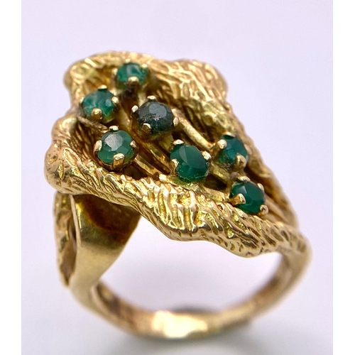 100 - A Vintage 18K Gold (tested) and Emerald Forest Ring. Seven green emerald blossoms sit amongst decora... 