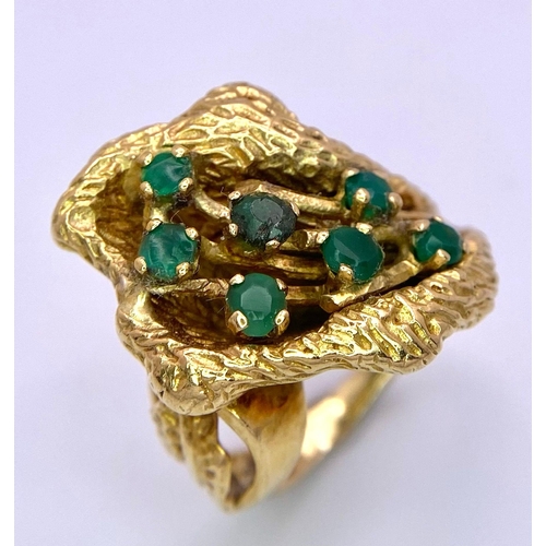 100 - A Vintage 18K Gold (tested) and Emerald Forest Ring. Seven green emerald blossoms sit amongst decora... 