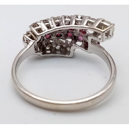 268 - An 18K White Gold Ruby and Diamond Crossover Ring. Six round cut rubies in-between two rows of round... 