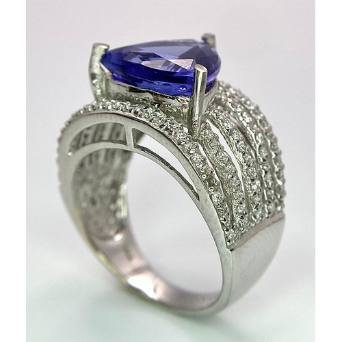 80 - An 18K White Gold, Tanzanite and Diamond Ring. Trillion cut tanzanite with a five row diamond arch f... 