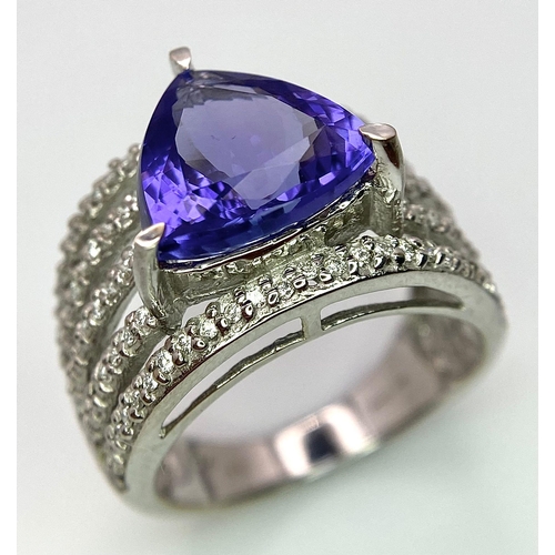 80 - An 18K White Gold, Tanzanite and Diamond Ring. Trillion cut tanzanite with a five row diamond arch f... 