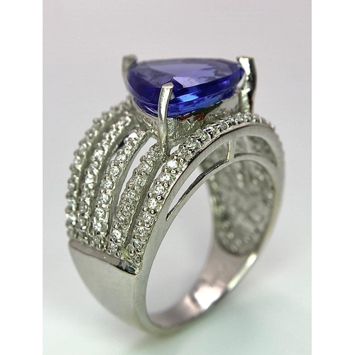 80 - An 18K White Gold, Tanzanite and Diamond Ring. Trillion cut tanzanite with a five row diamond arch f... 