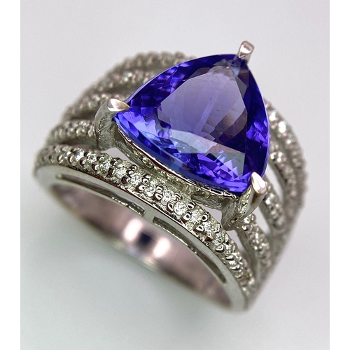 80 - An 18K White Gold, Tanzanite and Diamond Ring. Trillion cut tanzanite with a five row diamond arch f... 