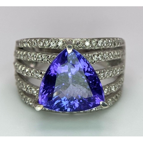 80 - An 18K White Gold, Tanzanite and Diamond Ring. Trillion cut tanzanite with a five row diamond arch f... 