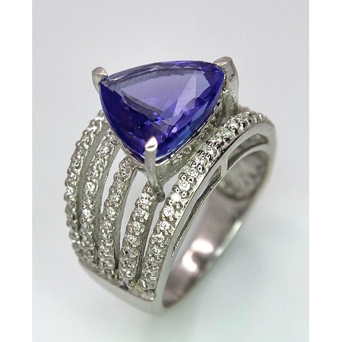 80 - An 18K White Gold, Tanzanite and Diamond Ring. Trillion cut tanzanite with a five row diamond arch f... 