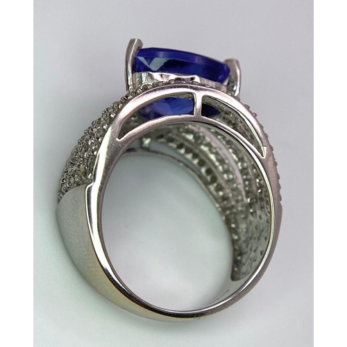 80 - An 18K White Gold, Tanzanite and Diamond Ring. Trillion cut tanzanite with a five row diamond arch f... 