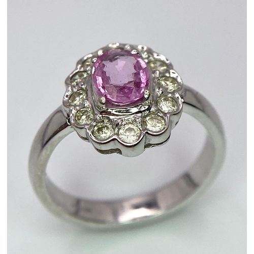 87 - A 9K White Gold, Diamond and Pink Sapphire Ring. Central oval cut pink sapphire with a diamond halo.... 