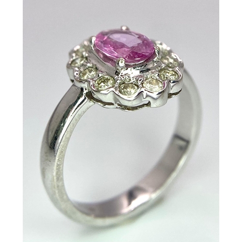 87 - A 9K White Gold, Diamond and Pink Sapphire Ring. Central oval cut pink sapphire with a diamond halo.... 