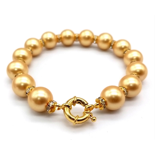 866 - A South Sea Pearl Shell Gold Tone Bead Bracelet. White stone spacers. Gilded clasp. 18cm