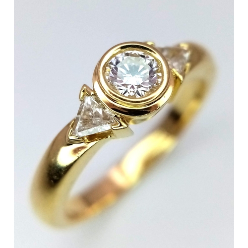 246 - An 18K Yellow Gold Diamond Ring. Central round cut diamond with trillion cut diamond accents. Size M... 