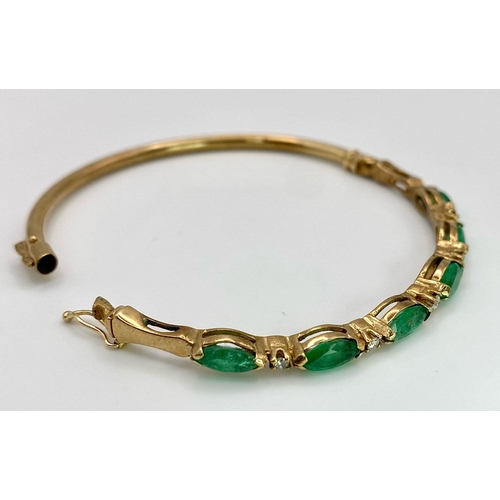 34 - A 9K Yellow Gold Emerald and Diamond Bangle. Six oval cut emeralds with five brilliant round cut dia... 