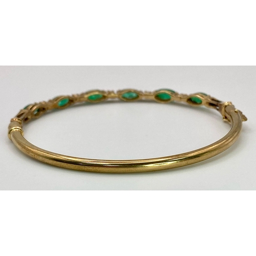 34 - A 9K Yellow Gold Emerald and Diamond Bangle. Six oval cut emeralds with five brilliant round cut dia... 