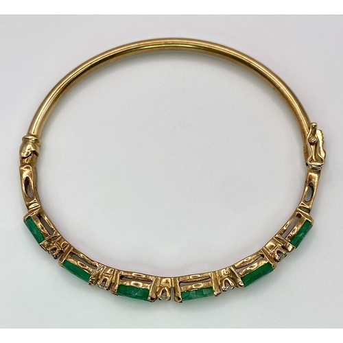 34 - A 9K Yellow Gold Emerald and Diamond Bangle. Six oval cut emeralds with five brilliant round cut dia... 