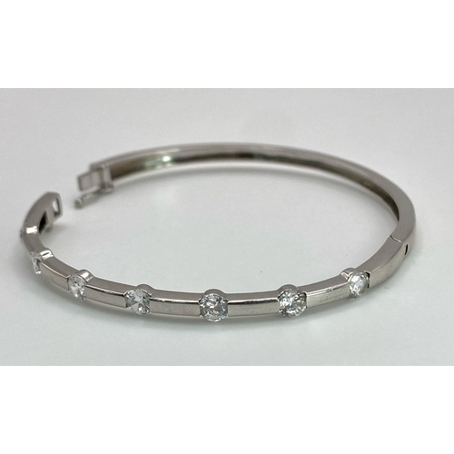 137 - A 9K White Gold and Diamond Bangle. Seven round cut diamonds with clip design. 56mm inner diameter. ... 