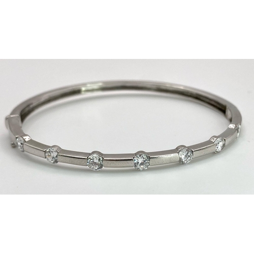 137 - A 9K White Gold and Diamond Bangle. Seven round cut diamonds with clip design. 56mm inner diameter. ... 