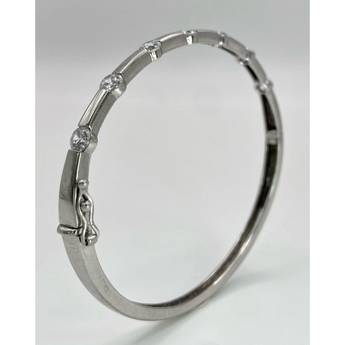 137 - A 9K White Gold and Diamond Bangle. Seven round cut diamonds with clip design. 56mm inner diameter. ... 