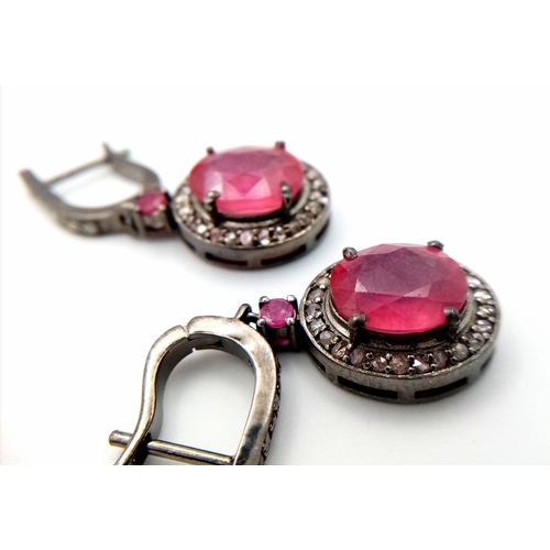 583 - A Pair of Ruby and Diamonds Earrings. Central oval ruby with a diamond surround in a classy gunmetal... 