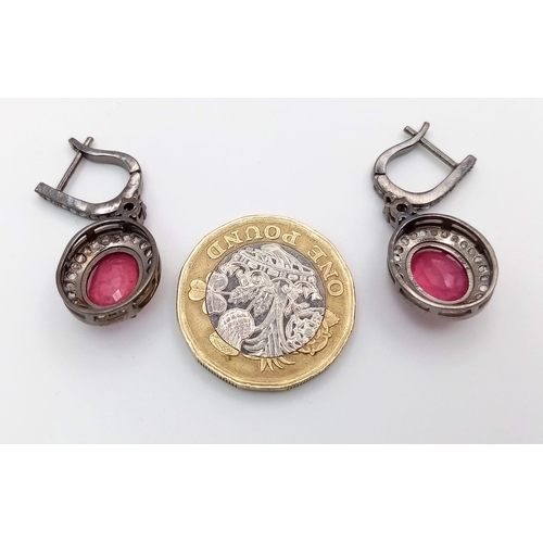 583 - A Pair of Ruby and Diamonds Earrings. Central oval ruby with a diamond surround in a classy gunmetal... 