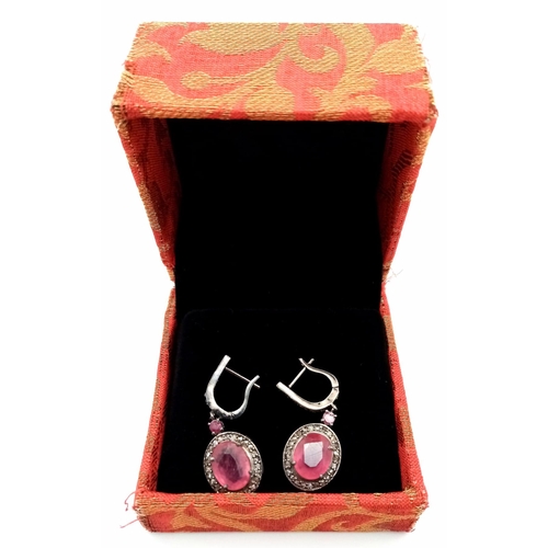 583 - A Pair of Ruby and Diamonds Earrings. Central oval ruby with a diamond surround in a classy gunmetal... 