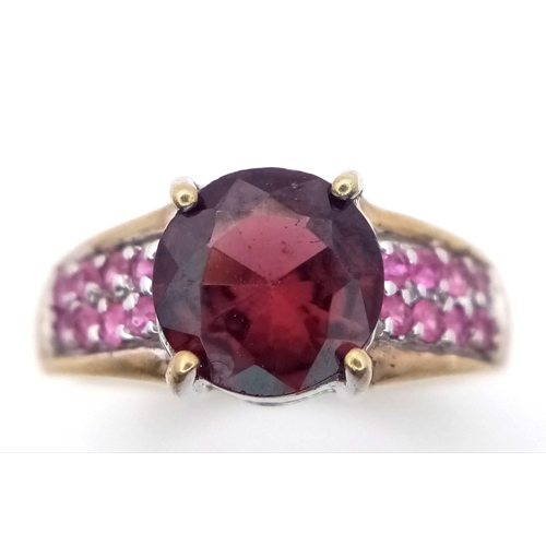 624 - A 9K Yellow Gold Garnet and Ruby Ring. Central garnet with ruby accents. Size K. 3.05g total weight.